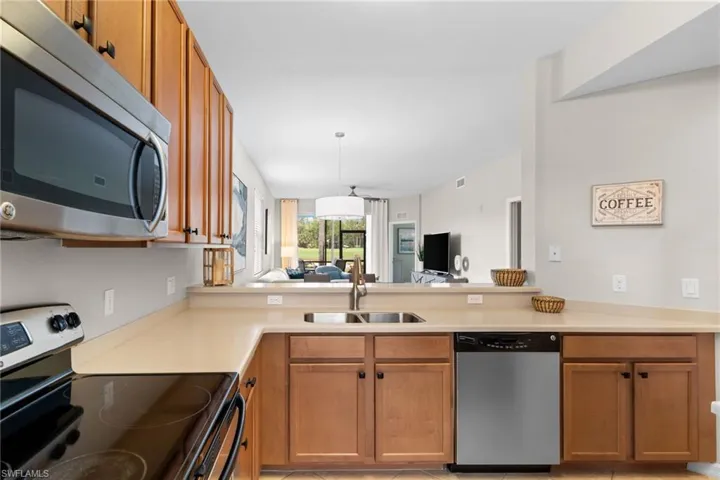 Kitchen featuring stainless steel appliances, light countertops, wood finish cabinetry, open floor plan, and pendant lighting