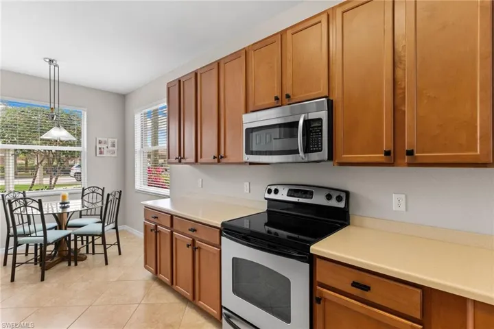 Kitchen featuring stainless steel appliances, light countertops, decorative light fixtures, and wood finish cabinetry