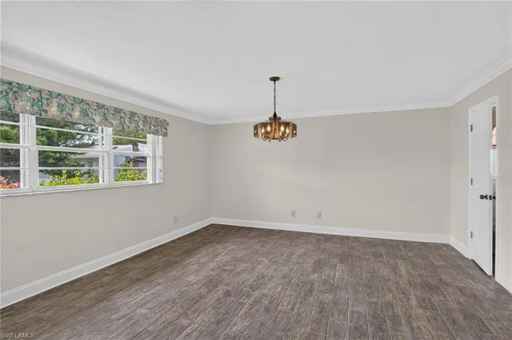 Wood-finish flooring, crown molding, and a chandelier illuminate this spacious room