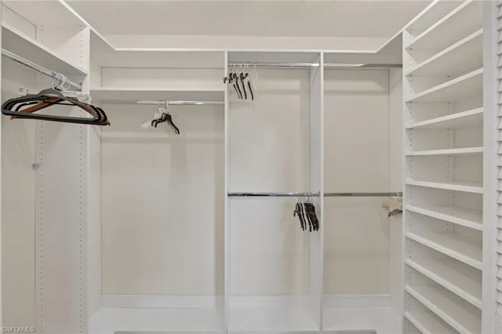 Built-in white storage system featuring multiple hanging rods, adjustable shelving, and louvered paneling