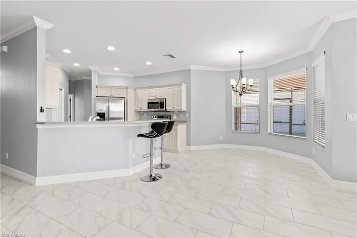 Kitchen featuring a breakfast bar, a chandelier, ornamental molding, appliances with stainless steel finishes, and pendant lighting