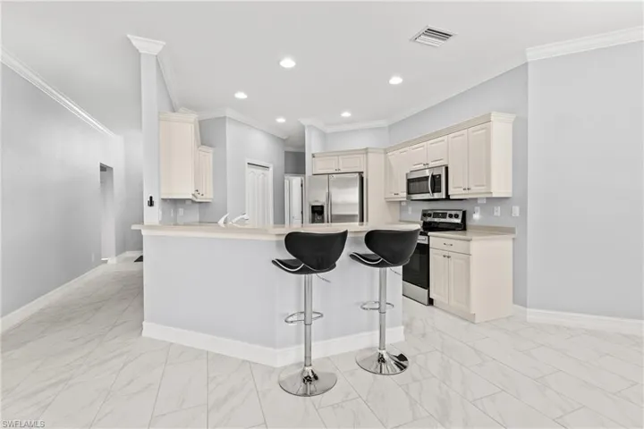 Kitchen with crown molding, stainless steel appliances, a center island, cream cabinets, and a kitchen bar