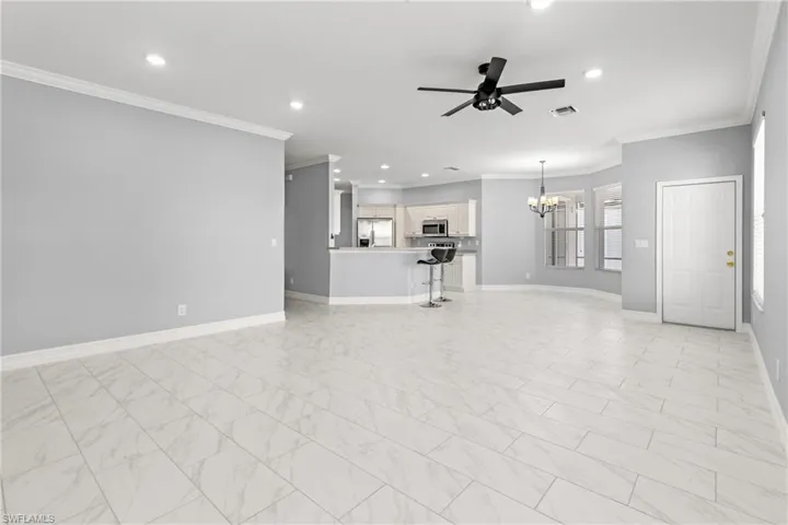 Unfurnished living room featuring ornamental molding and ceiling fan with notable chandelier