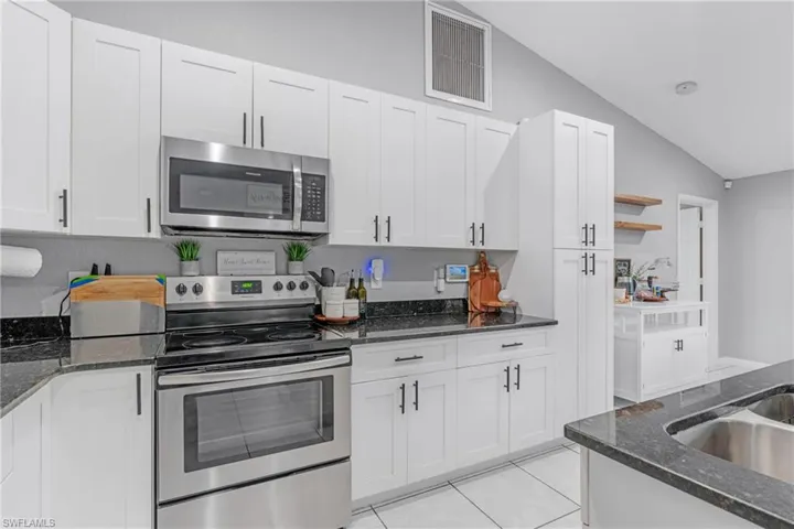 Kitchen with stainless steel appliances, white cabinets, and lofted ceiling