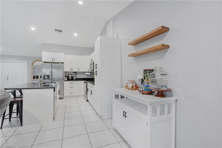 Kitchen with a center island with sink, light tile flooring, a breakfast bar, white cabinetry, and appliances with stainless steel finishes