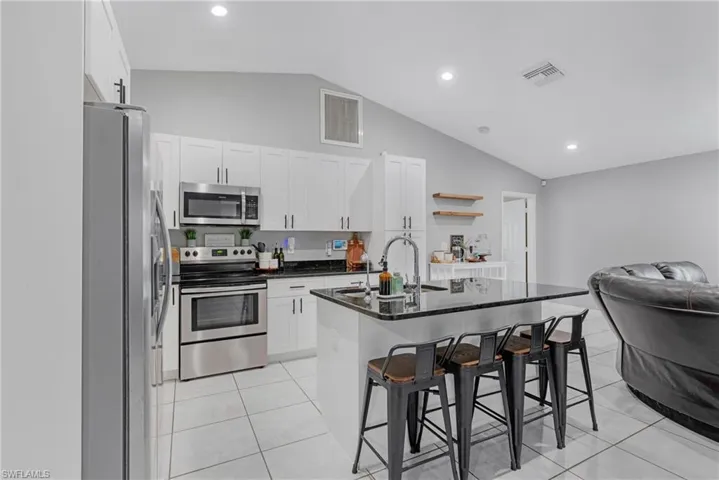 Kitchen featuring an island with sink, vaulted ceiling, sink, a breakfast bar, and appliances with stainless steel finishes