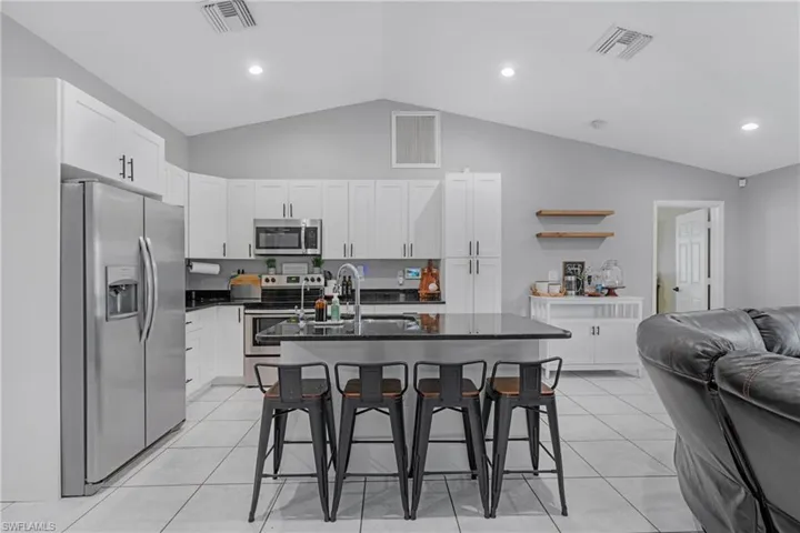 Kitchen with an island with sink, light tile floors, a breakfast bar, and stainless steel appliances