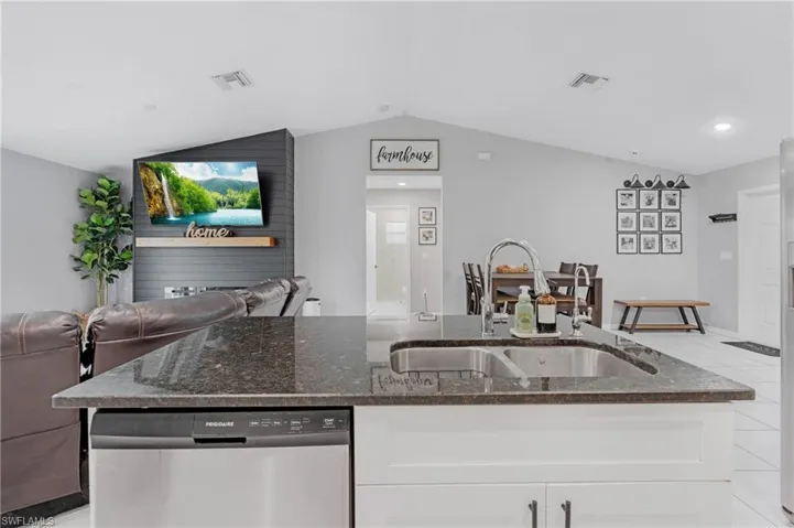 Kitchen with dishwasher, vaulted ceiling, light tile floors, sink, and white cabinets