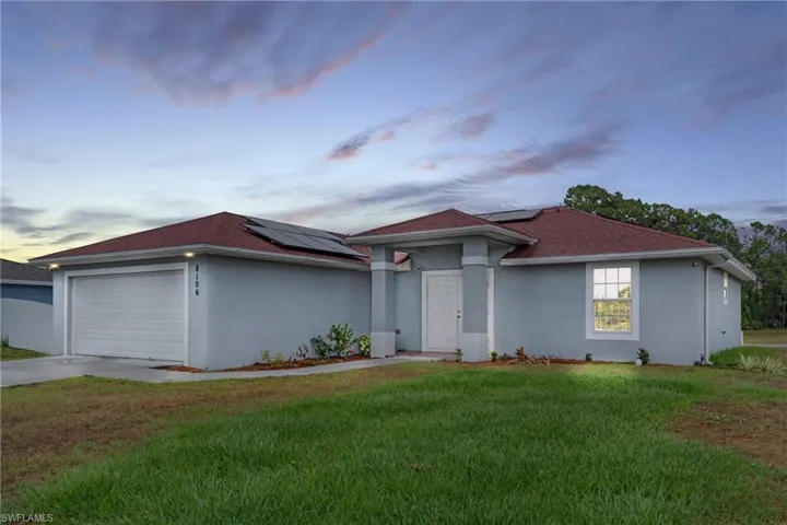 View of front of property with a garage, a lawn, and solar panels