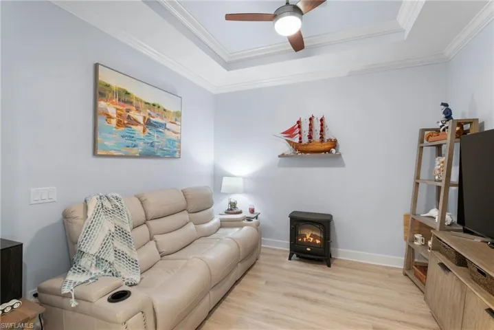 Living room featuring a wood stove, a tray ceiling, light hardwood / wood-style floors, ceiling fan, and ornamental molding