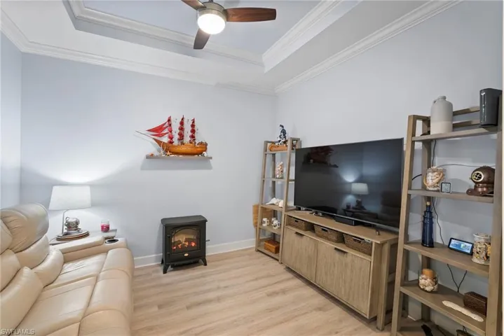 Living room featuring light hardwood / wood-style flooring, a wood stove, a raised ceiling, and crown molding