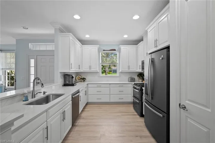Kitchen featuring appliances with stainless steel finishes, white cabinetry, light hardwood / wood-style flooring, ornamental molding, and sink