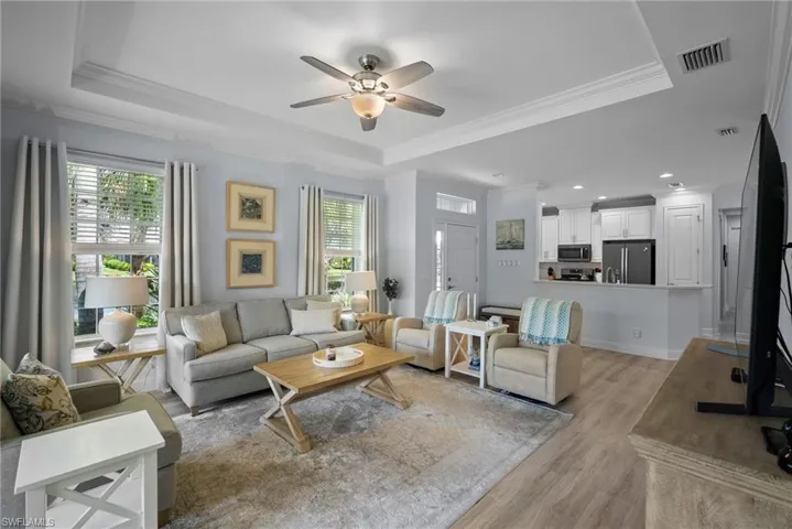 Living room featuring crown molding, a raised ceiling, light wood-type flooring, and ceiling fan