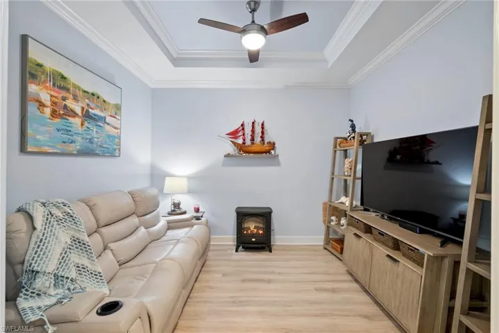 Living room with light hardwood / wood-style flooring, a tray ceiling, a wood stove, ornamental molding, and ceiling fan