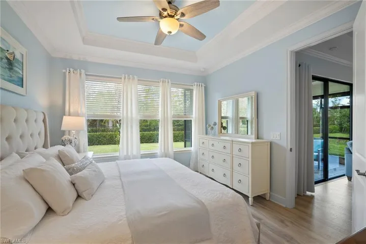 Bedroom with access to outside, crown molding, light wood-type flooring, a raised ceiling, and ceiling fan