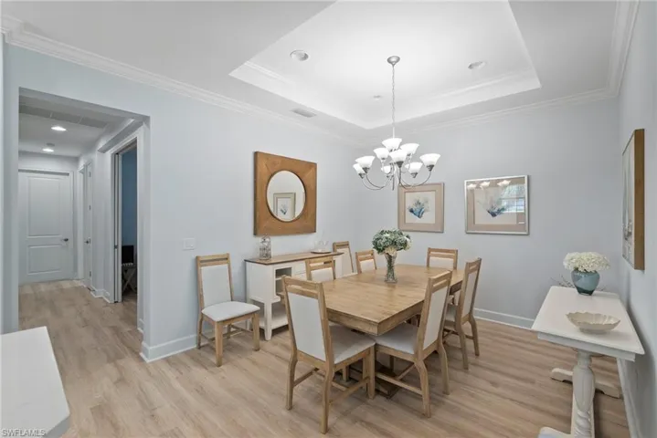 Dining space featuring an inviting chandelier, ornamental molding, a tray ceiling, and light wood-type flooring