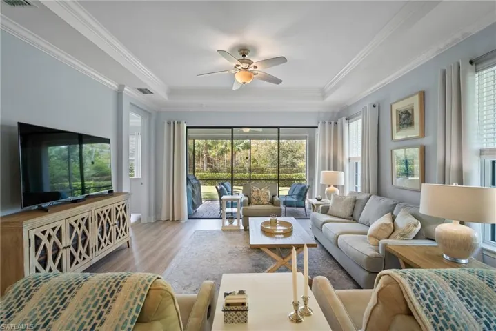 Living room with ornamental molding, a tray ceiling, light wood-type flooring, and ceiling fan