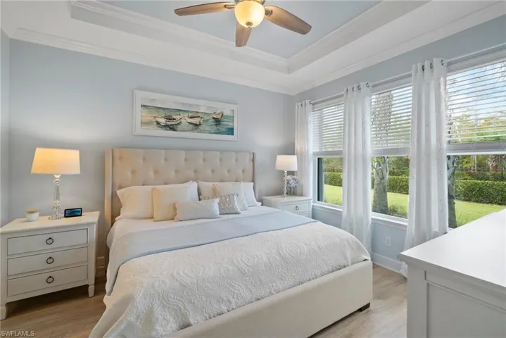 Bedroom featuring ornamental molding, a tray ceiling, light wood-type flooring, and ceiling fan