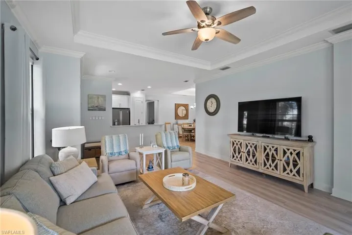 Living room with ornamental molding, light hardwood / wood-style flooring, a raised ceiling, and ceiling fan