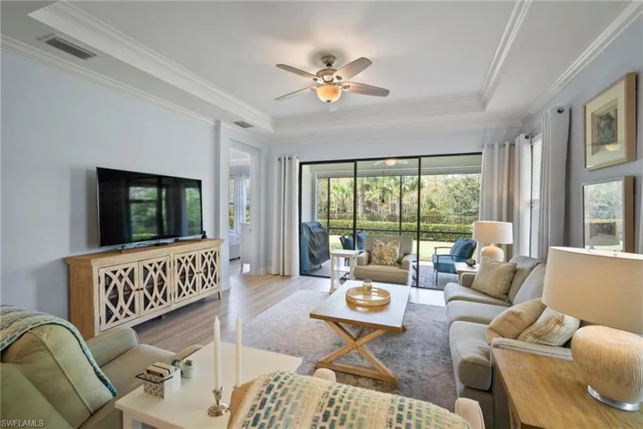 Living room featuring light hardwood / wood-style floors, crown molding, a raised ceiling, and ceiling fan