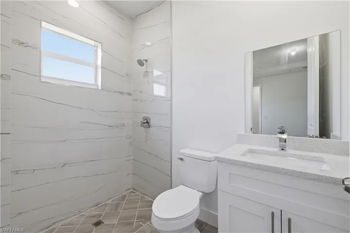 Primary Bathroom -Bathroom featuring a tiled shower with a window, a white toilet, and a vanity with an integrated sink and mirror