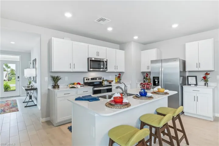 Kitchen featuring white cabinets, sink, a center island with sink, appliances with stainless steel finishes, and a kitchen breakfast bar