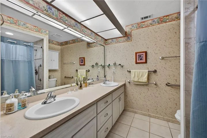 Bathroom with curtained shower, wallpapered walls, double vanity, and light tile patterned floors