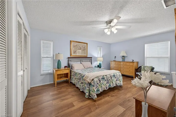 Bedroom featuring two closets, multiple windows, wood finished floors, a ceiling fan, and a textured ceiling