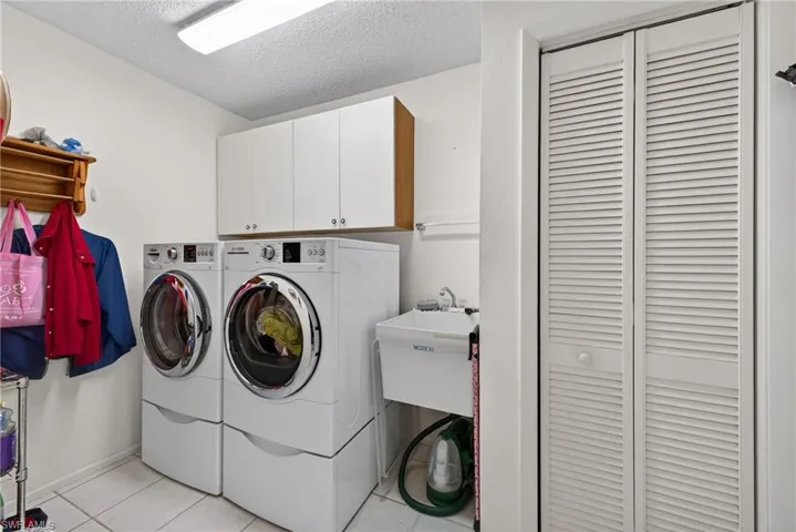 Laundry area featuring a textured ceiling, separate washer and dryer, cabinet space, and light tile patterned floors
