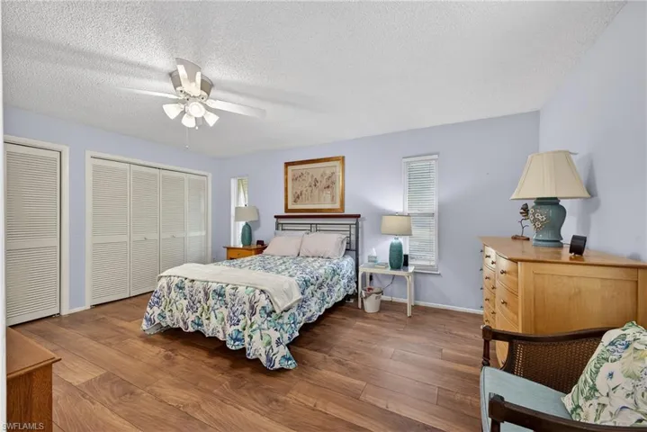 Bedroom featuring multiple closets, dark wood finished floors, a textured ceiling, ceiling fan, and multiple windows