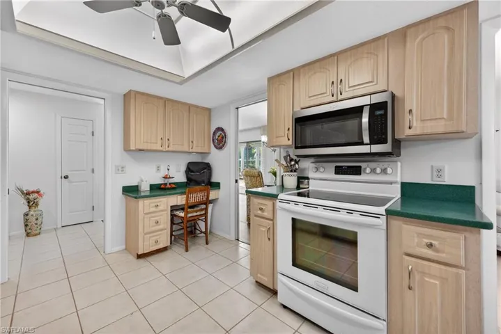 Kitchen featuring white range with electric stovetop, dark countertops, light brown cabinets, and built in study area