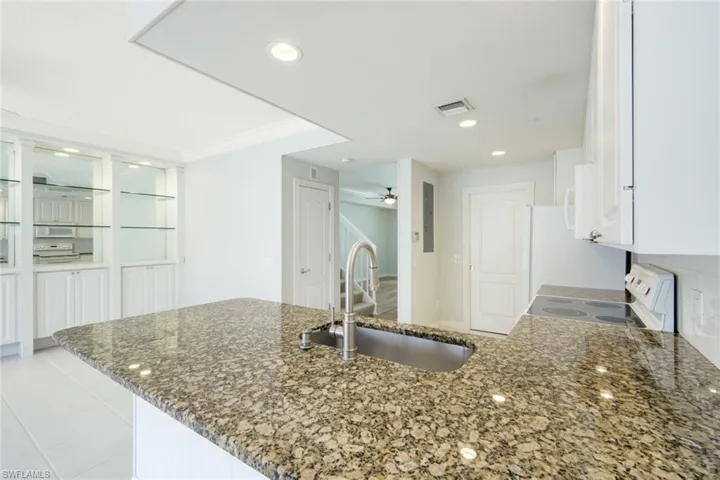 Kitchen featuring a speckled granite countertop, undermount stainless steel sink with gooseneck faucet, white cabinetry, and recessed lighting