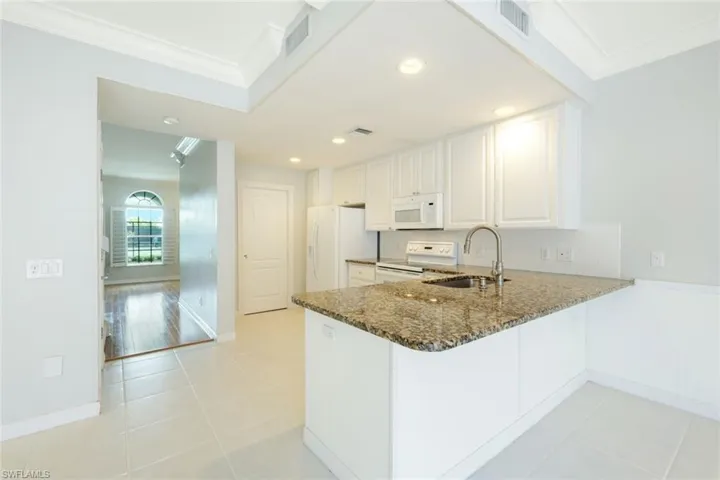 Kitchen featuring white cabinetry, a granite-finish island with an undermount sink, white appliances, and tiled flooring
