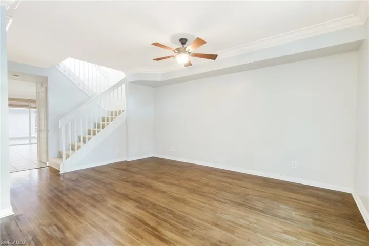 Spacious living area featuring wood-finish flooring, a ceiling fan, and crown molding