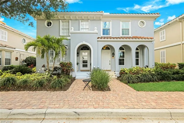 Stucco exterior featuring arched entryways, a terracotta tile roof, white-framed windows, and circular accent windows