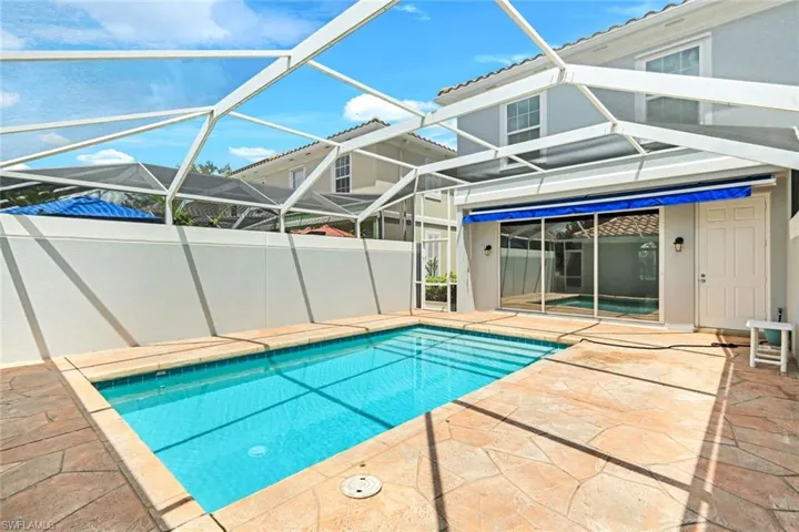 Screened-in pool area featuring a rectangular pool, flagstone-patterned deck, privacy wall, and direct access to the interior via sliding glass doors