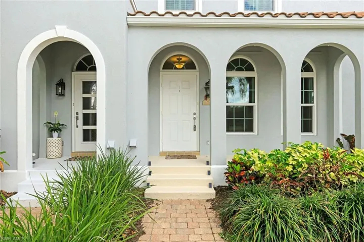 Stucco exterior featuring multiple archways, a white paneled entry door with decorative glass inserts, and arched windows with gridded panes