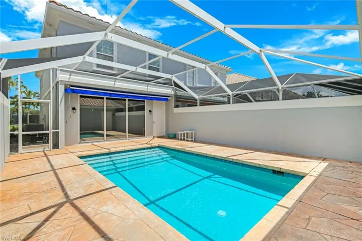 Screened pool enclosure featuring a rectangular swimming pool, textured patio decking, and a covered patio area with retractable awning