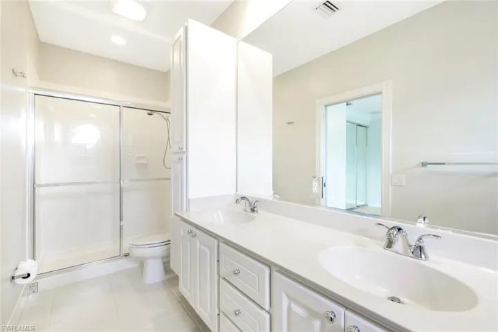 Double vanity with white cabinetry and integrated sinks, chrome fixtures, a large mirror, and tiled flooring