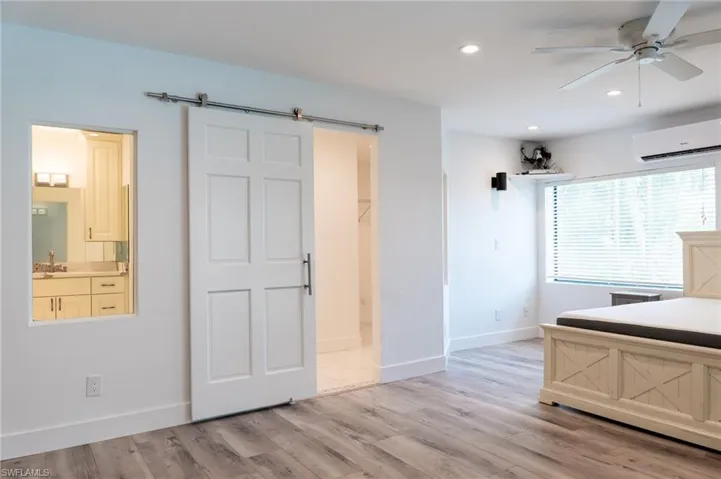 Bedroom with a barn door, a wall unit AC, light wood finished floors, baseboards, and recessed lighting