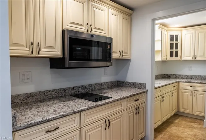 Kitchen featuring light stone counters, stainless steel microwave, black electric stovetop, glass insert cabinets, and cream cabinets