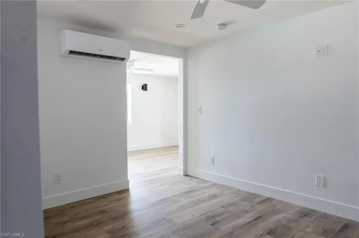 Spare room featuring ceiling fan, an AC wall unit, wood finished floors, and baseboards