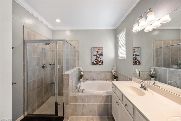 Primary Bathroom featuring double vanity, a garden tub, a stall shower, and ornamental molding