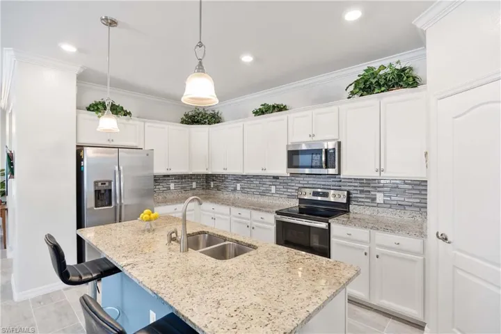 Kitchen featuring white cabinets, stainless steel appliances, ornamental molding, pendant lighting, and decorative backsplash