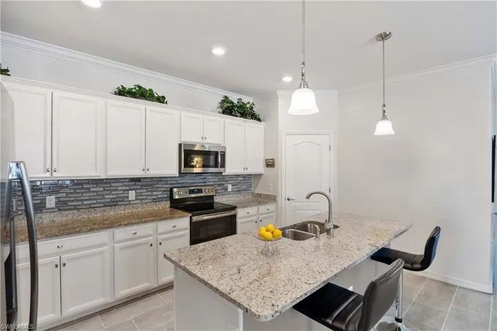 Kitchen with white cabinets, stainless steel appliances, light stone countertops, a breakfast bar area, and ornamental molding