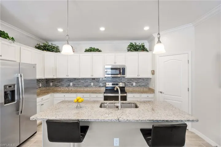 Kitchen with stainless steel appliances, white cabinetry, decorative backsplash, a kitchen breakfast bar, and an island with sink