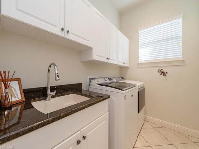 Washroom featuring a sink, baseboards, independent washer and dryer, cabinet space, and light tile patterned floors