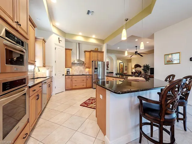 Kitchen with a sink, stainless steel appliances, backsplash, wall chimney exhaust hood, and visible vents
