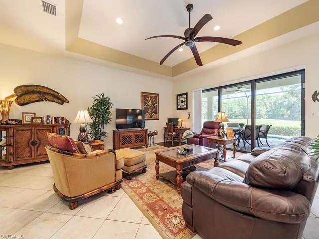 Living room featuring light tile patterned floors, ceiling fan, a tray ceiling, visible vents, and recessed lighting