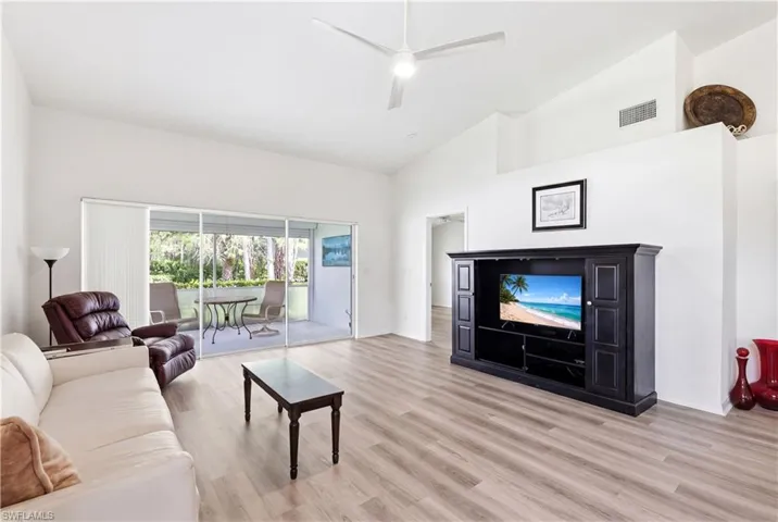 Spacious living area featuring high vaulted ceilings, light wood-finish flooring, and a large sliding glass door opening to a screened patio